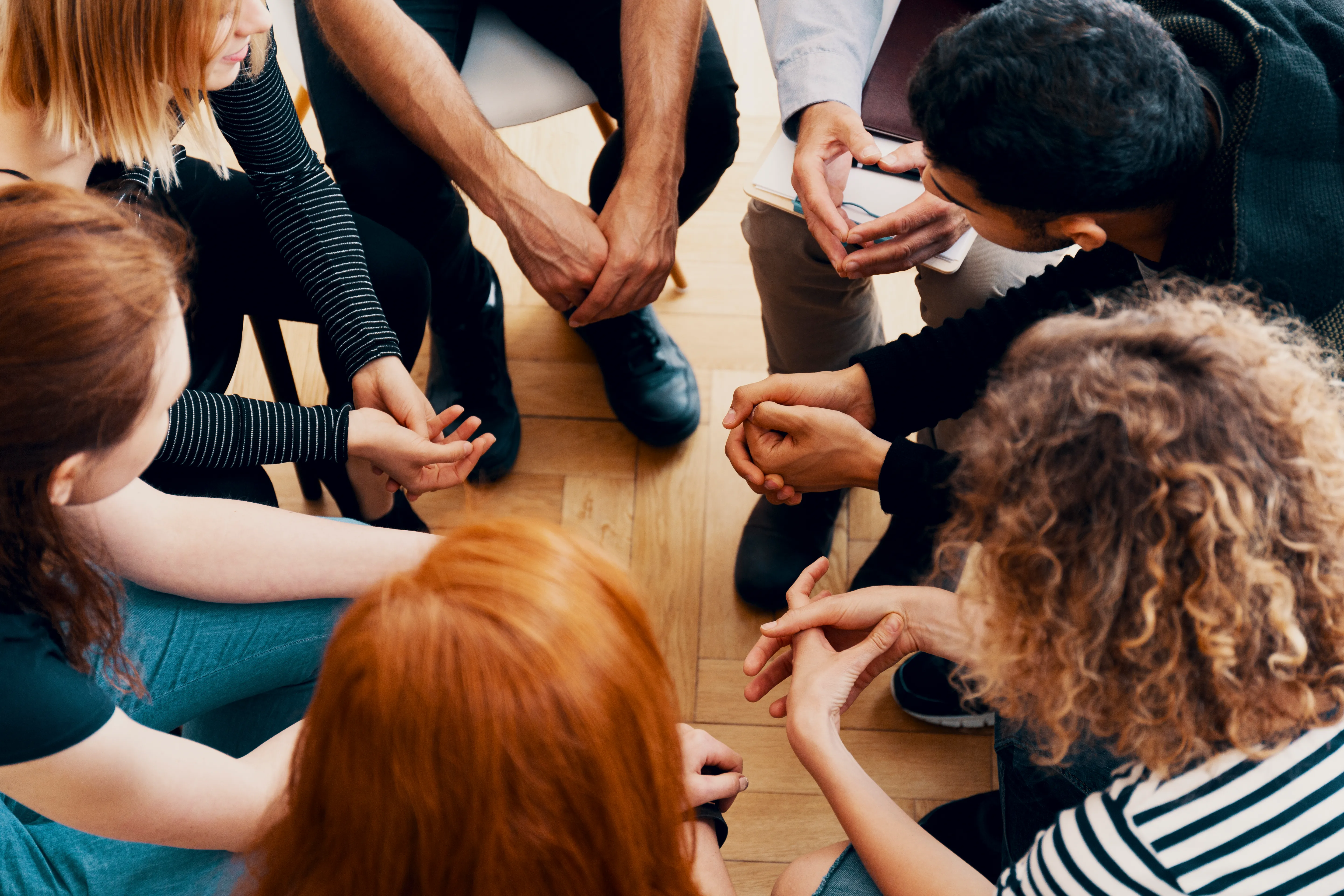 A group of people sitting in a circle, hands meeting in the middle